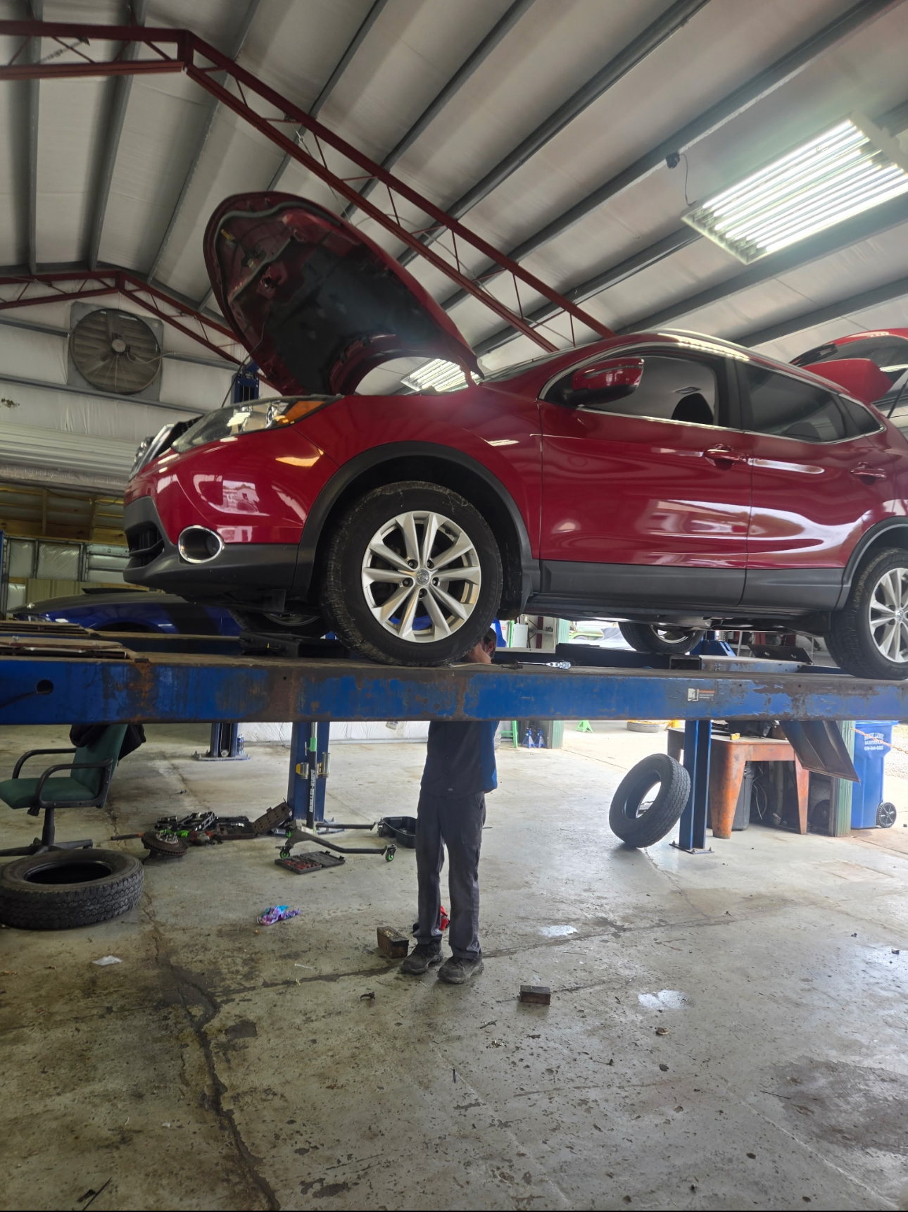 Red SUV on the lift with mechanic working underneath, hood open
